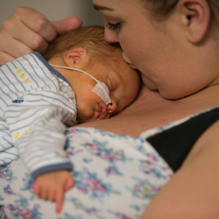 Mum holding baby on her chest while kissing baby's forehead