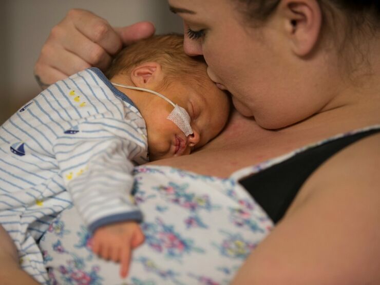 Mum holding baby on her chest while kissing baby's forehead