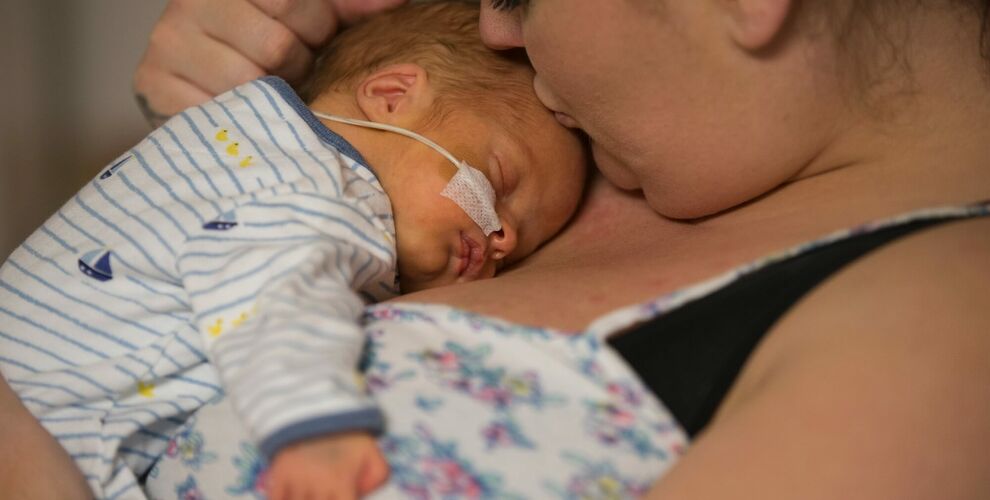 Mum holding baby on her chest while kissing baby's forehead