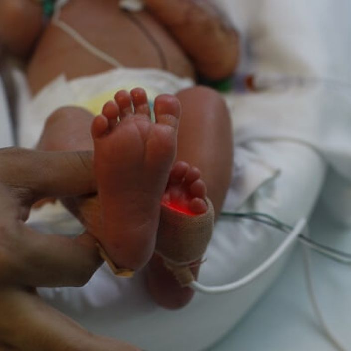 Parent holding premature baby's foot in hospital