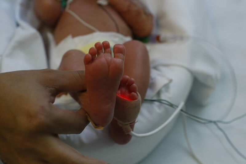 Parent holding premature baby's foot in hospital