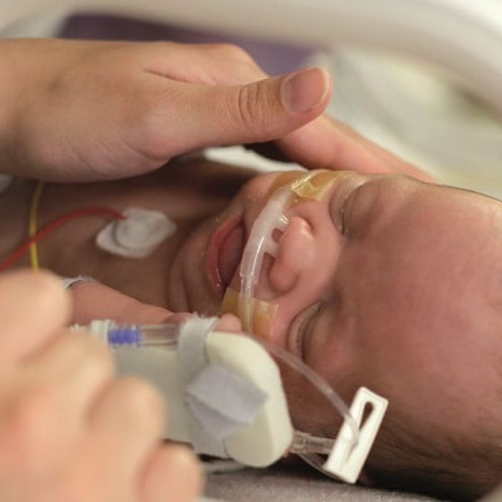 Parent comforting sleeping baby attached to tubes in incubator