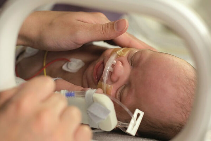 Parent comforting sleeping baby attached to tubes in incubator