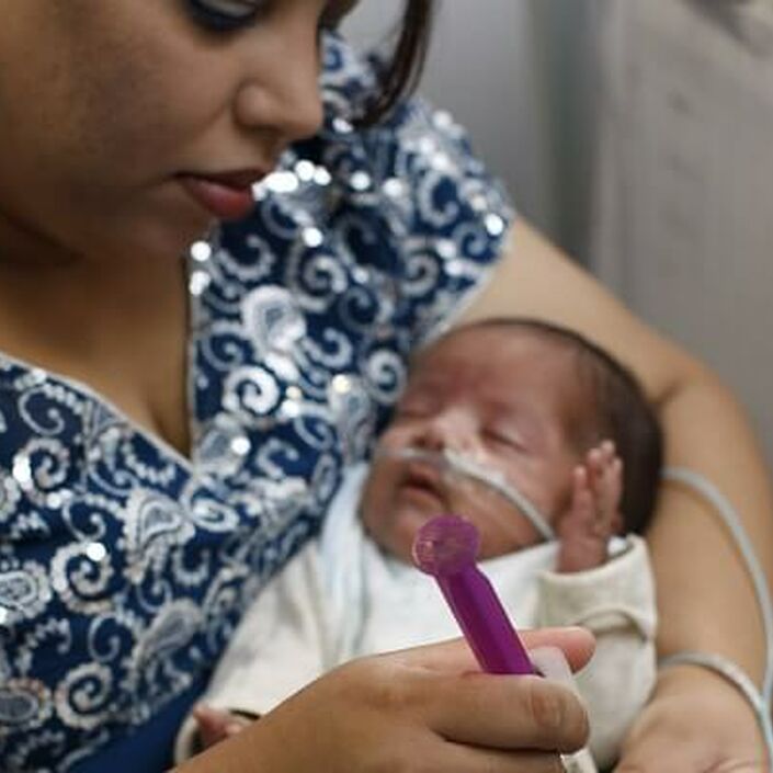 Mum holding baby in her arms while tube feeding her
