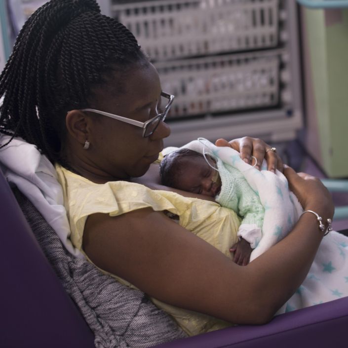 Mum reclining in a hospital chair with her baby wrapped in blanket and resting on her chest