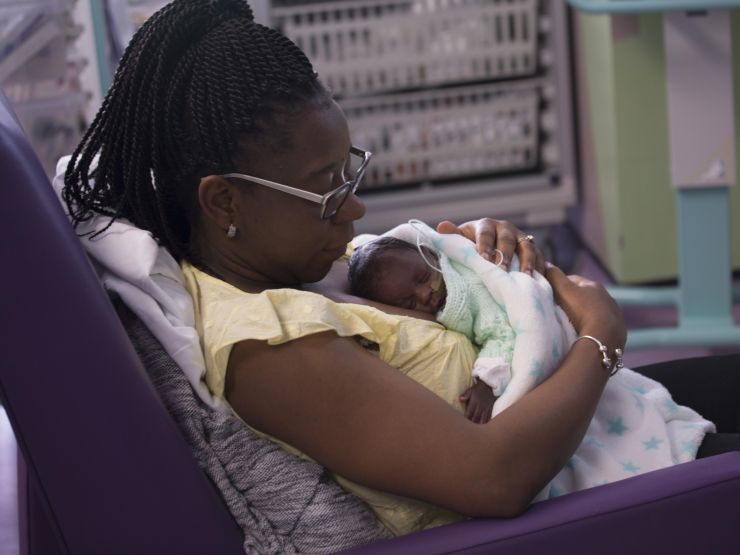Mum reclining in a hospital chair with her baby wrapped in blanket and resting on her chest