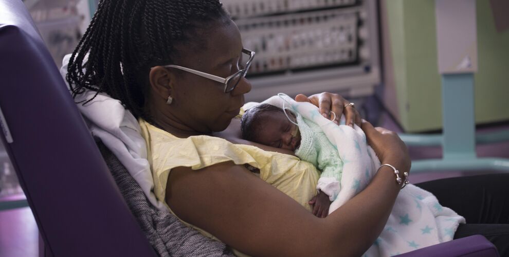 Mum reclining in a hospital chair with her baby wrapped in blanket and resting on her chest