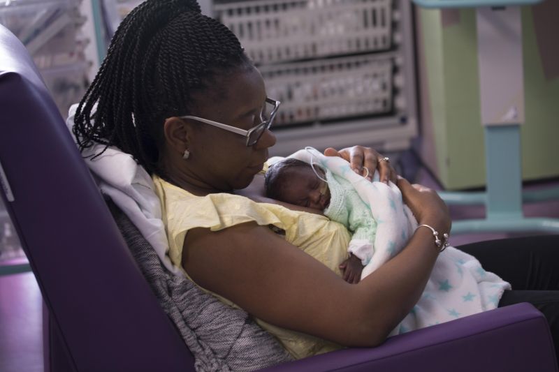Mum reclining in a hospital chair with her baby wrapped in blanket and resting on her chest
