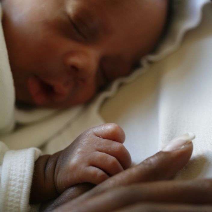 Baby asleep lying on their front holding onto parent's finger