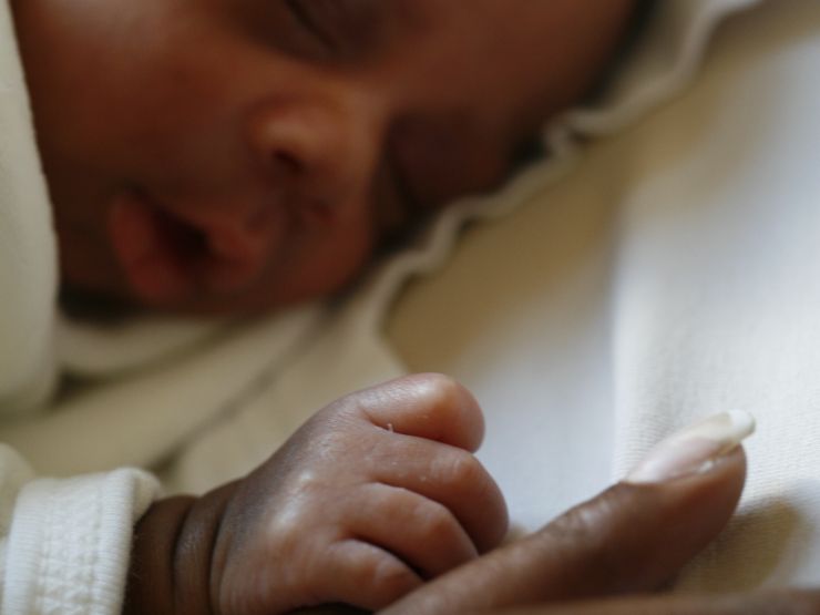 Baby asleep lying on their front holding onto parent's finger