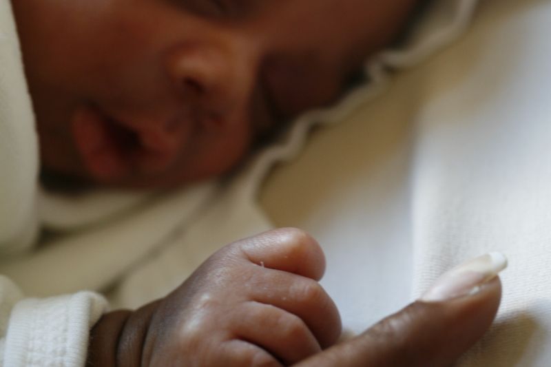 Baby asleep lying on their front holding onto parent's finger
