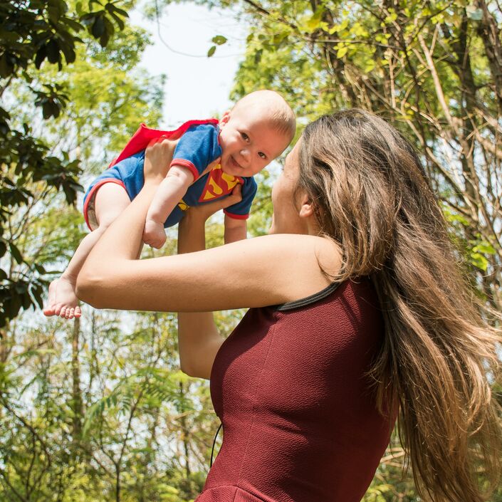 Mum lifting baby up dressed as superman in a wooded area