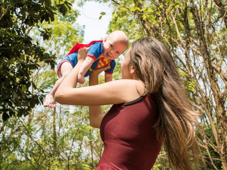 Mum lifting baby up dressed as superman in a wooded area