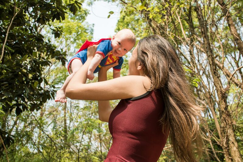 Mum lifting baby up dressed as superman in a wooded area