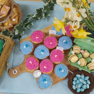 Colourful cakes displayed on a table, some with pink or blue frosting
