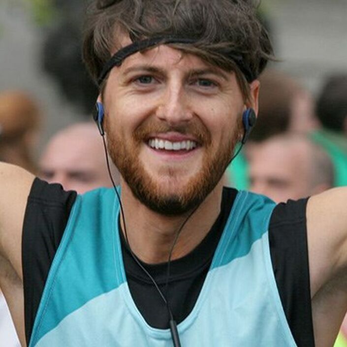 Head shot of man running celebrating with arms in the air at an event wearing a Bliss running vest