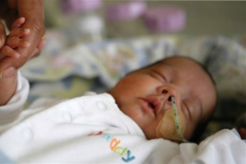 Adult holding hand of premature baby in neonatal care