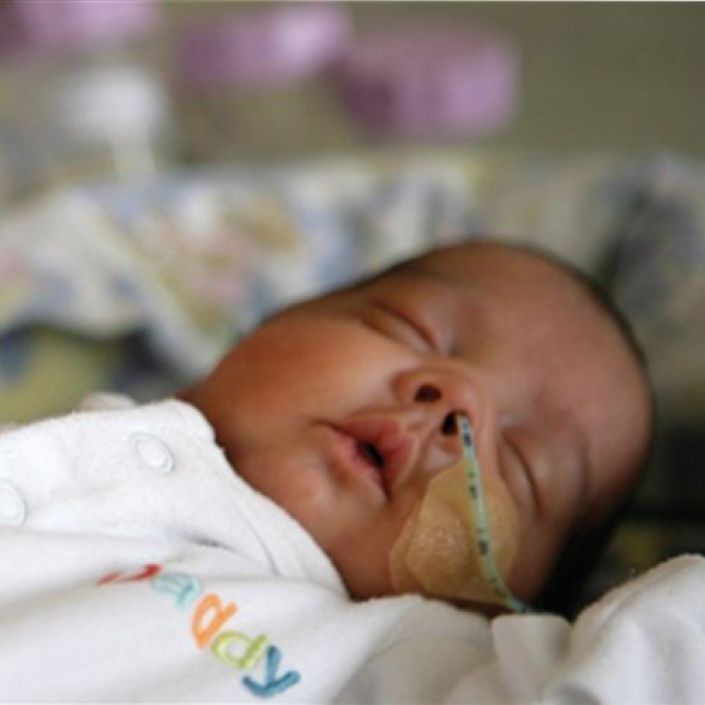 Adult holding hand of premature baby in neonatal care