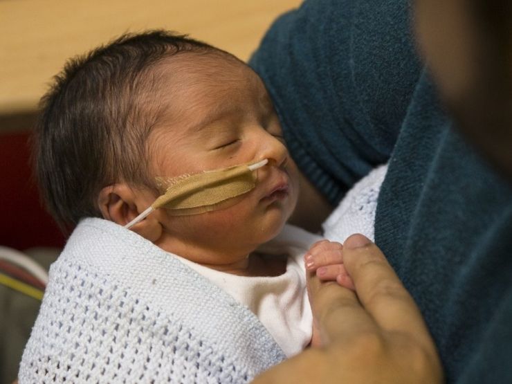 Baby in neonatal care attached to a feeding tube being held by his father