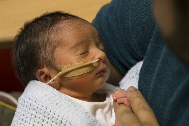 Baby in neonatal care attached to a feeding tube being held by his father