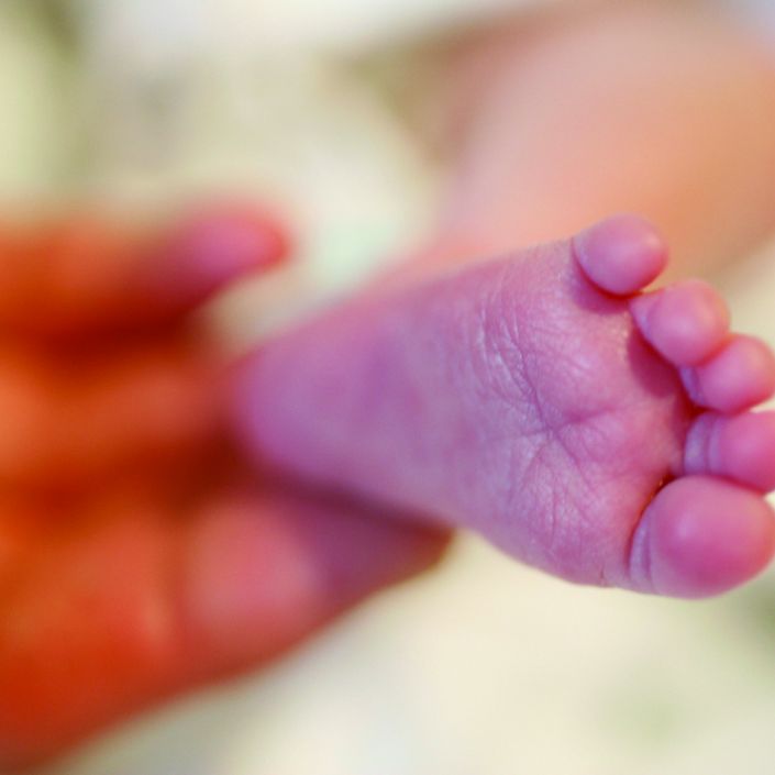 Baby's foot in focus being held by a hand which is blurred in the background