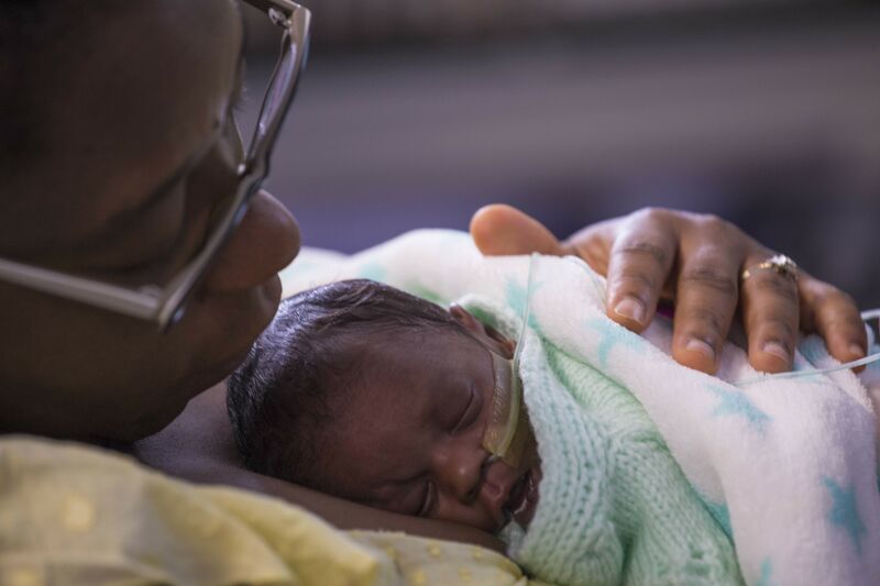 Mum holding baby on her chest looking at the baby wrapped in blankets. Baby is asleep.