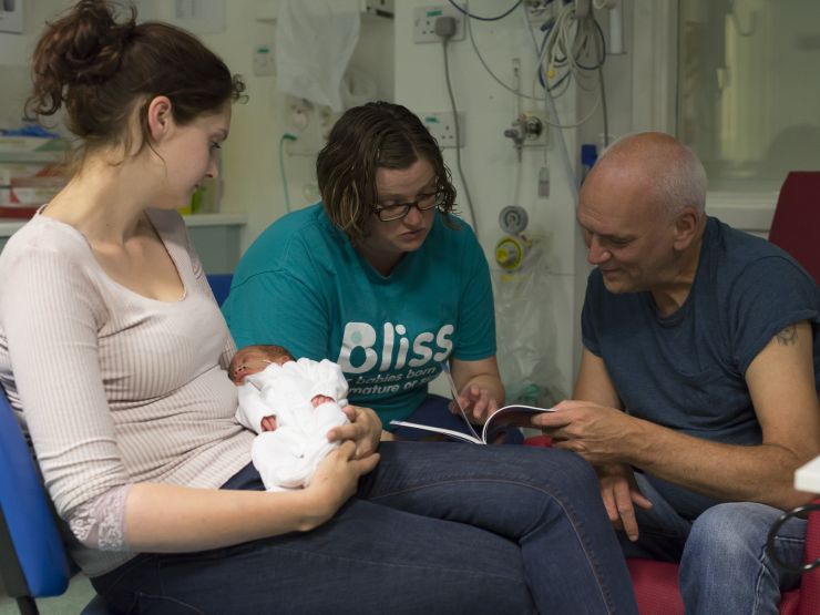 Bliss volunteer with family members and baby looking at information together in a neonatal unit