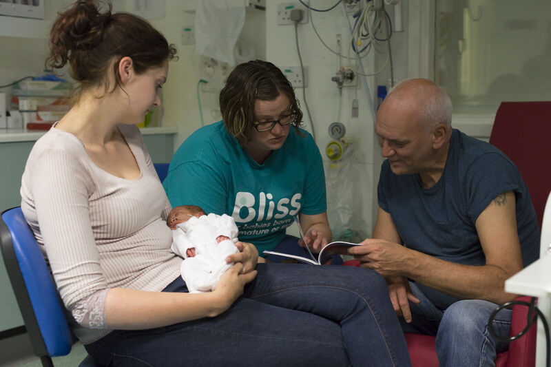 Bliss volunteer with family members and baby looking at information together in a neonatal unit