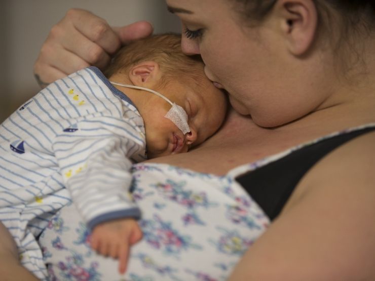 Mum with baby on chest who is asleep and mum is giving the baby a kiss