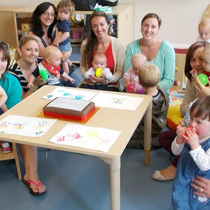 Group of mums and babies with Bliss volunteers sitting around a table in a play area
