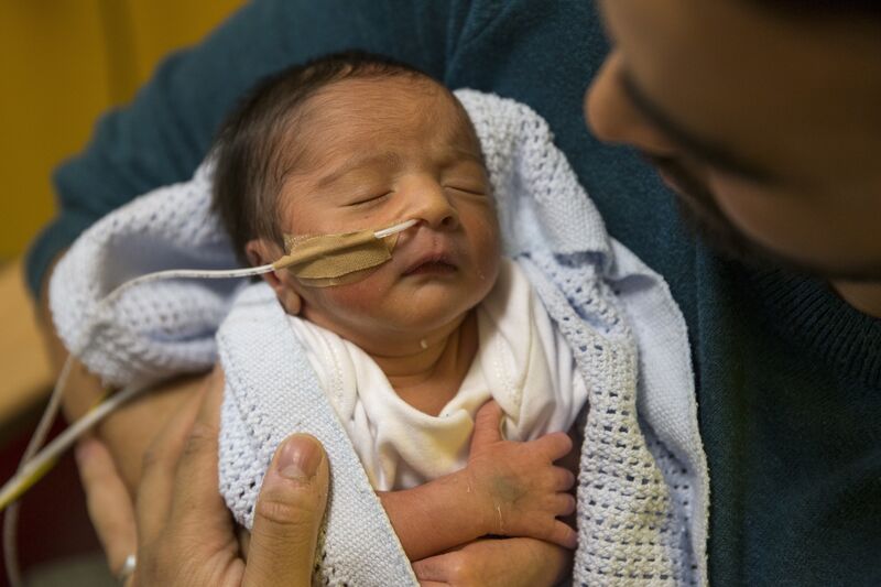 Baby wrapped in blanket being tube fed while dad holds him in his arms