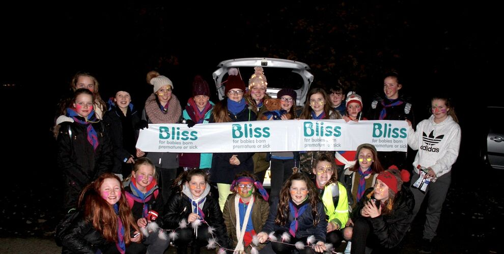 Group of Girl Guides standing in a group in the dark decorated with face paints and wearing torches and fairy lights