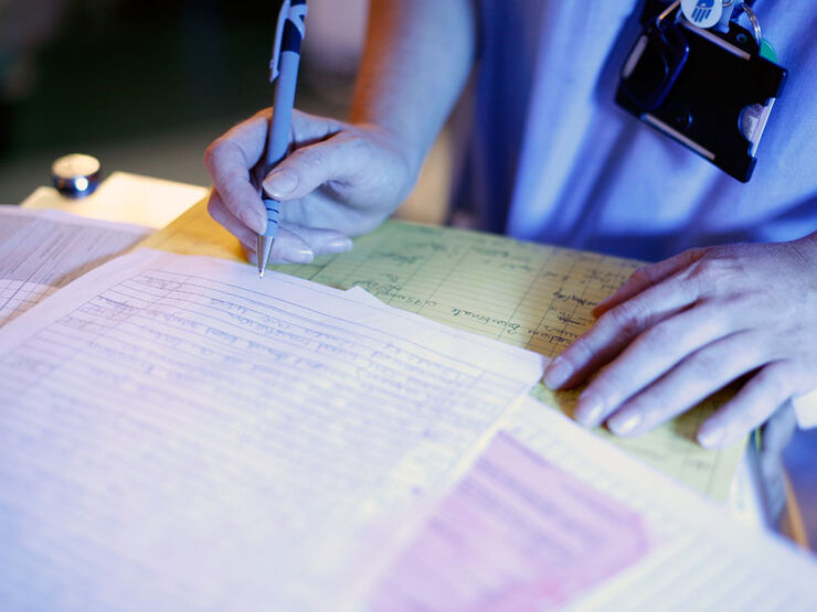 Close up of nurse holding a pen over several paper documents laid out on a desk