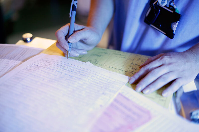 Close up of nurse holding a pen over several paper documents laid out on a desk