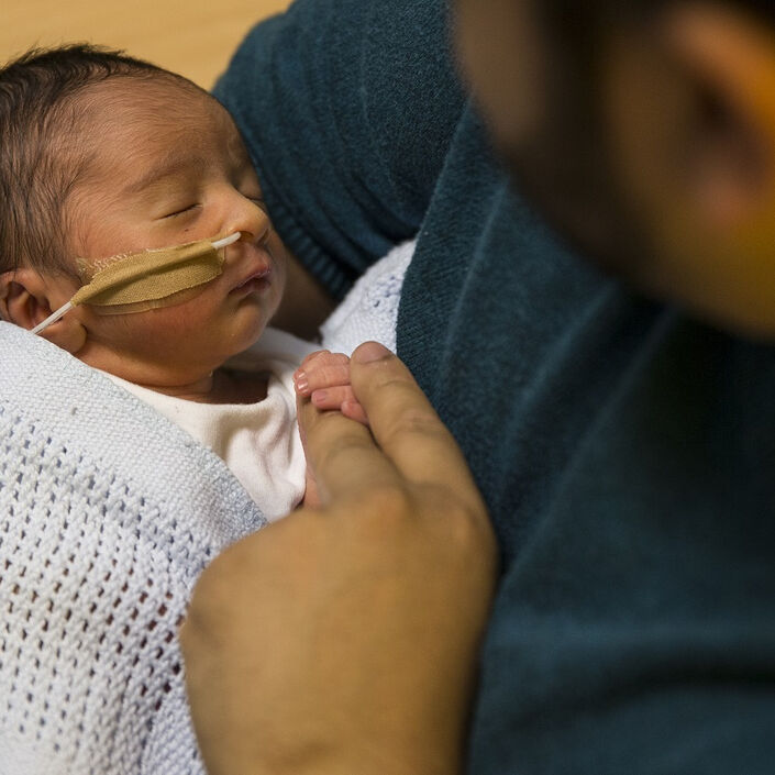 Baby with tube attached to nose holding dad's finger