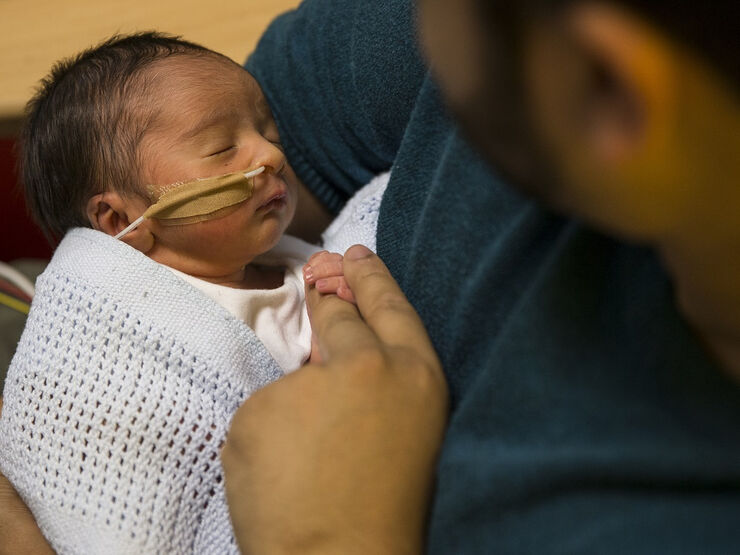 Baby with tube attached to nose holding dad's finger