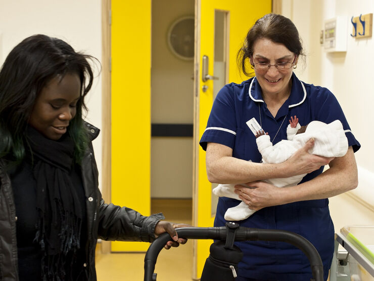 Mum getting the pram ready while a nurse holds her baby
