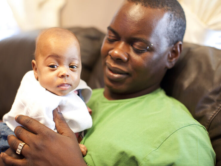Dad sat on the sofa holding his baby looking at him lovingly