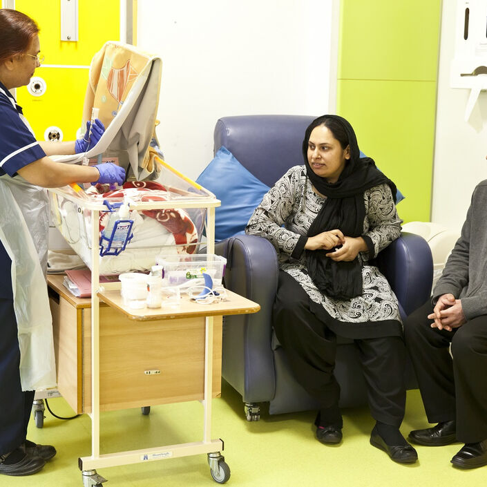 Nurse tube feeding a baby in a cot while the parents sit nearby