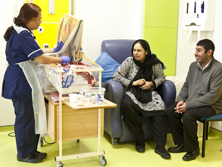 Nurse tube feeding a baby in a cot while the parents sit nearby