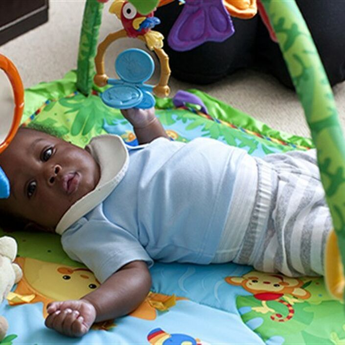 Baby lying on the floor on his back looking at the camera surrounded by toys