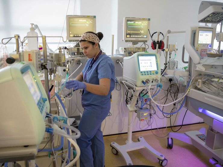 Neonatal nurse stands next to incubator look at the instrument readings