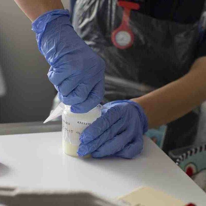 Healthcare professional with latex gloves on opening a bottle of medicine