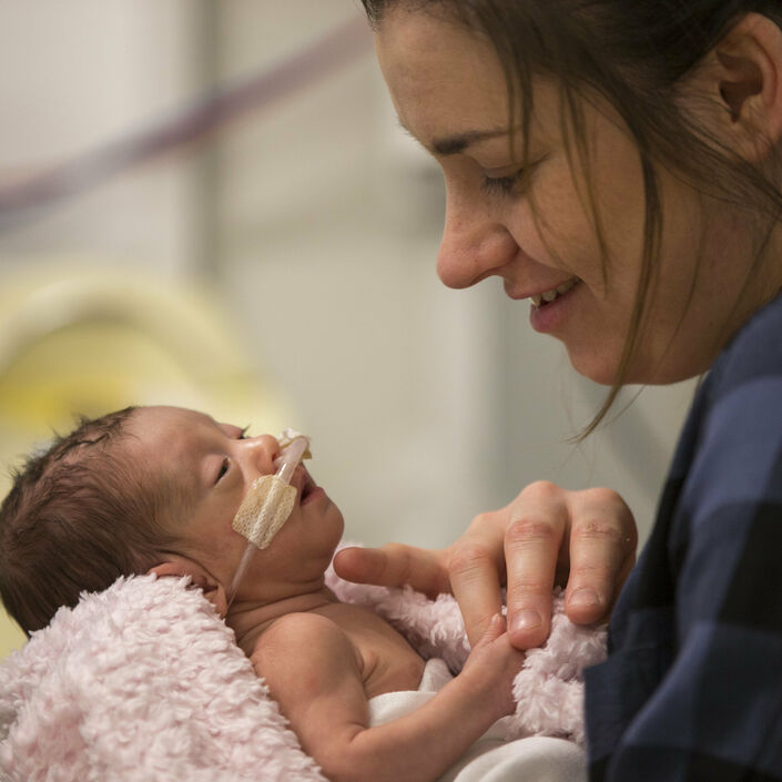 Premature baby attached to tubes being held and admired by mother