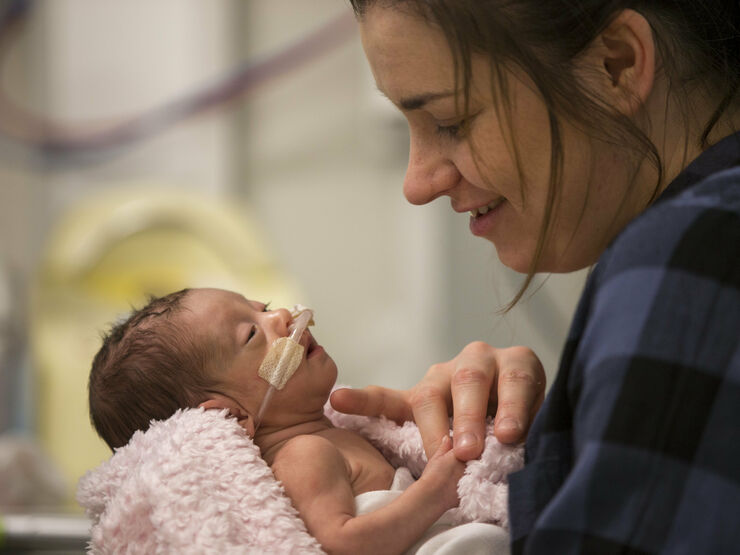 Premature baby attached to tubes being held and admired by mother