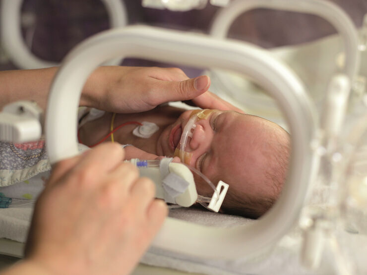 Mum caressing premature baby in an incubator. Baby attached to various tubes