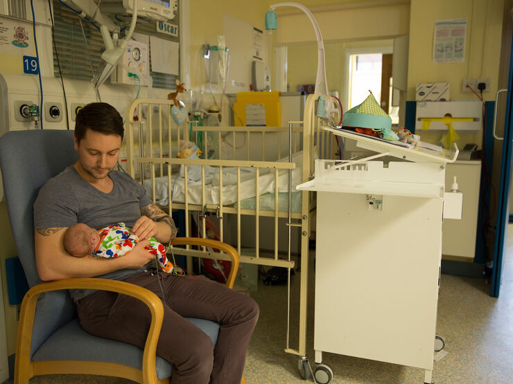 Father holding his baby in a chair next to a cot in an neonatal unit