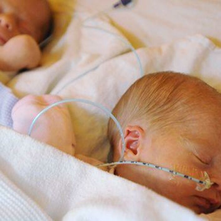 Twin babies wrapped in blankets sleeping side by side with tubes attached