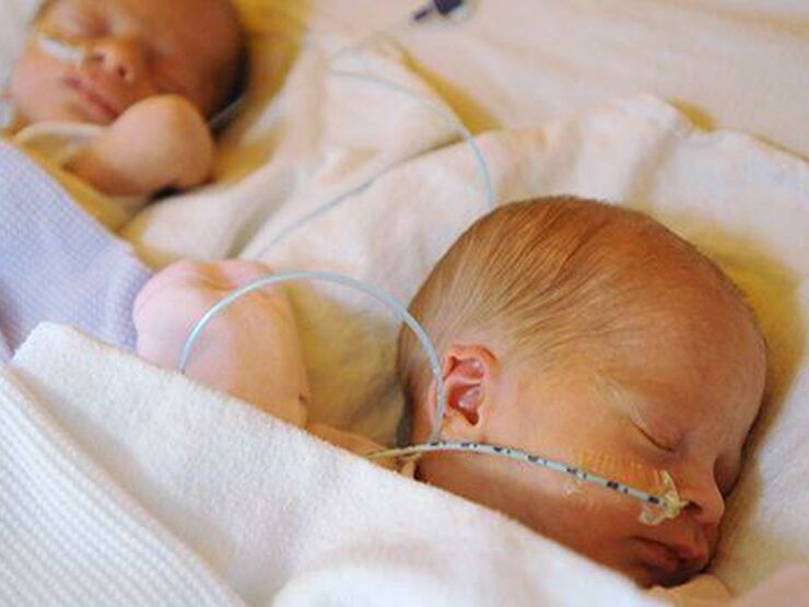 Twin babies wrapped in blankets sleeping side by side with tubes attached