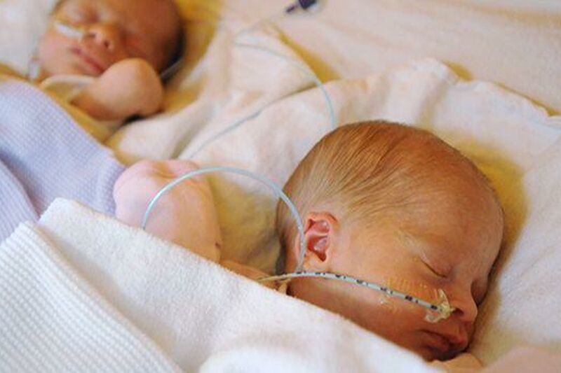 Twin babies wrapped in blankets sleeping side by side with tubes attached